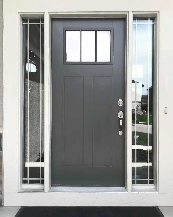 A black door with a silver handle and 3 small equal windows at the top
